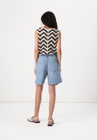 Černobílý cropped top pletený se vzorem chevron, doplněný světle denimovými šortkami s elastickým pasem a dvěma zadními kapsami.