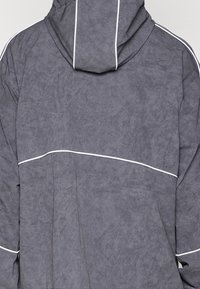 Gray hooded jacket with a textured fabric, featuring white piping along the seams and a relaxed fit. No visible hardware or logos.