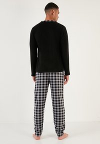 Top negro de manga larga combinado con pantalones de pijama a rayas grises y negros, con una textura suave y un corte relajado, visto desde la parte trasera.