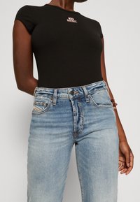 Bodysuit negro de manga corta con el logo rosa de Diesel, combinado con unos pantalones de mezclilla de tiro alto en azul claro que presentan detalles desgastados y acentos de costura.