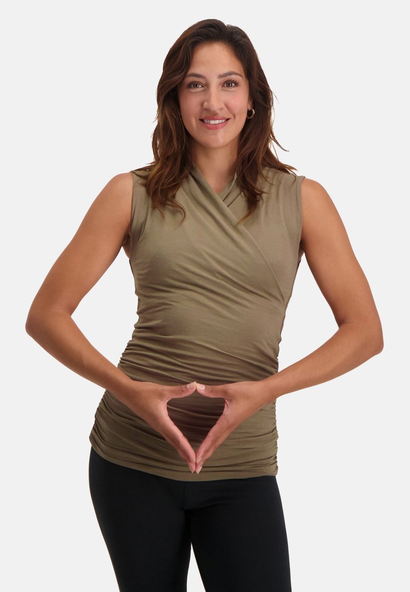 Ärmlös topp i olivgrön färg med en insvängd design, som har en samlad textur och en åtsittande silhuett. Kombinerad med svarta leggings.