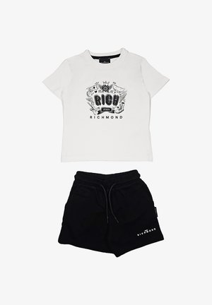 T-shirt bianco in cotone con grafica nera e testo "RICH", abbinata a pantaloni corti neri in cotone con vita elastica e dettaglio del logo.