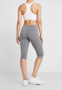 Biała sportowa biustonosz z plecami w kształcie racerback oraz szare legginsy, wykonane z elastycznego materiału, cechujące się dopasowanym krojem i elastycznym pasem w talii.