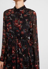 Schwarzes, durchsichtiges Kleid mit floralem Muster in Rot, Weiß und Gelb, mit geknöpftem Vorderteil, Kragen und taillierter Taille. Lange Ärmel.
