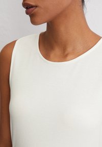 Weißes ärmelloses Oberteil mit einer weichen Textur und einem runden Ausschnitt, das eine glatte Oberfläche und ein minimalistisches Design aufweist.