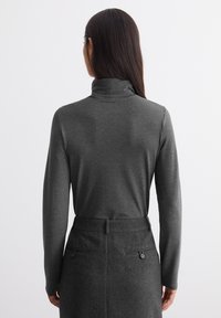 Graues langärmliges Rollkragenshirt, glatte Textur, taillierte Passform, kombiniert mit einem passenden grauen maßgeschneiderten Rock mit Seitentaschen und Knöpfen.