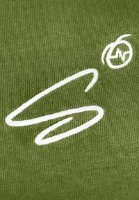 Tessuto verde con una finitura strutturata che presenta un design ricamato bianco in evidenza, inclusa una lettera stilizzata e un elemento circolare.