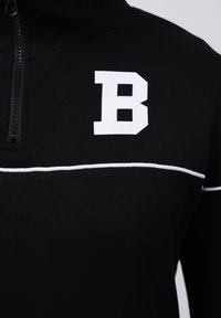 Black zip-up sweatshirt featuring a white horizontal stripe and a prominent white "B" logo on the left chest. Smooth, fitted fabric.