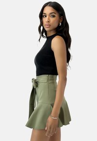 Top sin mangas de canalé negro combinado con una falda corta de talle alto en color verde oliva con un dobladillo acampanado y detalle de lazo en la parte delantera.