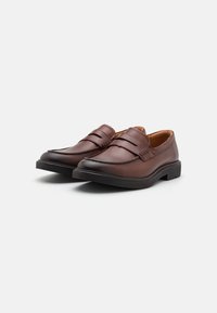 Mocassins en cuir marron avec une finition lisse, un bout arrondi, des accents à double bride, et une semelle en caoutchouc noire robuste.