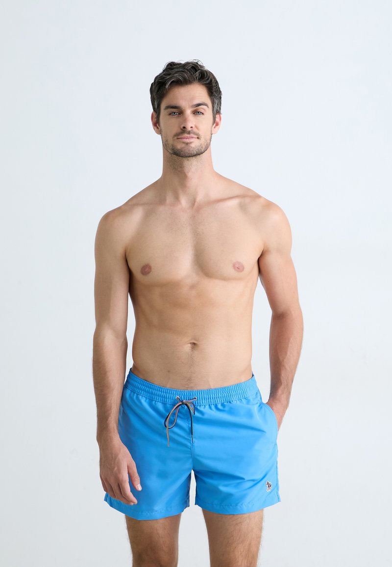 Un short de bain bleu avec une taille élastique et un cordon de serrage, ainsi qu'un petit patch logo sur la jambe gauche. Tissu lisse et léger.