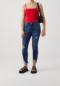 Červený top bez rukávů s tenkými ramínky, spárovaný s roztrhanými modrými džínami s třepenými lemy a výřezy. Černé sandály s pásky.