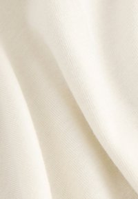 Tessuto color crema con una texture liscia e motivo a maglia fine, che mostra morbide pieghe e sottili variazioni di tonalità.