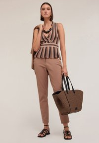Top fără mâneci, cu dungi maro și bej, cu un tiv peplum, asortat cu pantaloni bej mulati și o geantă de umăr cu model. Sandale cu bretele.