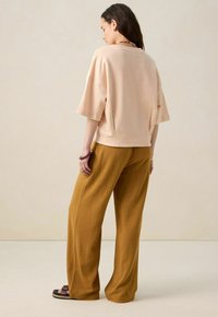 Haut pêche à manches courtes avec une coupe décontractée, associé à un pantalon large moutarde. Les deux matériaux semblent doux et décontractés, adaptés pour un style de vie relax.