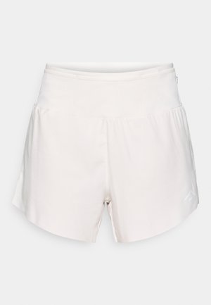 Pantalones cortos deportivos beige claro con una cintura elástica, dobladillo curvado y un pequeño logo blanco en el lado derecho. Textura de tela suave.