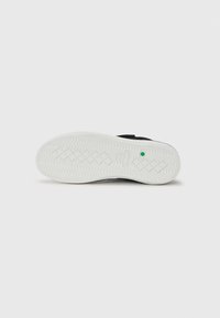 Black sneaker sole with a textured white rubber outsole, featuring a wave pattern and a small green accent near the heel area.