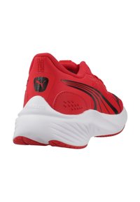 Zapatilla deportiva roja con parte superior de tela, acentos negros y suela blanca con un diseño texturizado; destacada por su talón acolchado y logotipo.