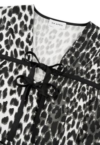 Czarnobiała bluzka w panterkę z dekoltem w kształcie litery V, ozdobiona czarną kokardą i kontrastującą czarną lamówką wzdłuż krawędzi. Widoczna metka marki.