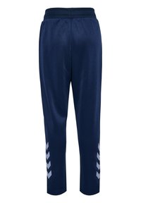 Marineblå atletikbukser med elastisk talje, tilspidsede ben og hvide chevronstriber nær anklerne på en ensfarvet baggrund.