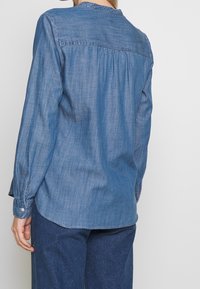 Camicia di jeans a maniche lunghe di blu medio, con dettagli sulla spalla e polsini con bottoni. Tessuto morbido con vestibilità rilassata e orlo curvo.