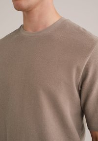 Khaki srajca s kratkimi rokavi z rebrasto teksturo in okroglim izrezom, ki ima gladko tkanino in sproščeno prileganje.