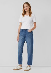 Biela krátka košeľa s krátkym rukávom, vysoko pásové modré džínsy, skrátená dĺžka s rozstrapkaným okrajom, skombinované s béžovými a bielymi teniskami.