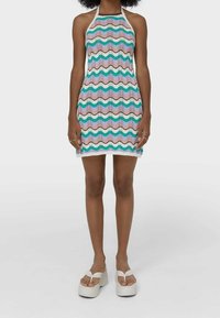 Kolorowa sukienka na halter z falistym wzorem w odcieniach różu, zieleni, bieli i niebieskiego. Dzianinowa struktura, długość powyżej kolan i białe wykończenie u dołu.