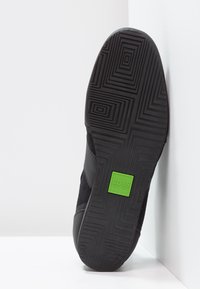 Black sneaker featuring a textured rubber sole, mesh upper, and a distinctive green BOSS logo on the heel. Geometric tread pattern on sole.