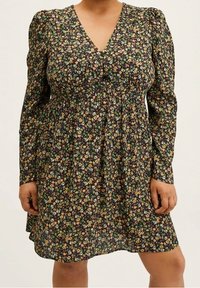 Robe longue à manches longues à motif floral avec un profond décolleté en V, fond sombre, petites fleurs colorées, taille smockée et silhouette fluide.