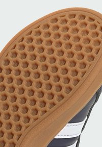 Suela de zapato de goma marrón con un patrón hexagonal, que presenta un borde biselado suave y detalles laterales en franjas blancas sobre un fondo oscuro.