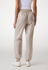 Lichtbeige satijnen joggers met een elastische tailleband, taps toelopende boorden en een subtiel patroon. Gemaakt om te dragen met witte sneakers.