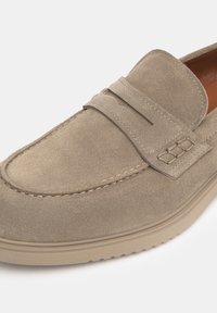 Mocassins en daim de couleur taupe clair avec un détail cousu et un accent rehaussé sur la bande. Dotés d'une semelle en beige rembourrée pour le confort.
