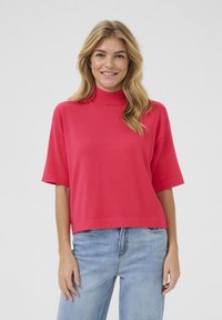 Short-sleeve, high-neck top in bright pink fabric. Loose fit with a straight hem, paired with light blue denim jeans.