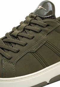 Olivově zelené tenisky z nubukového materiálu, kulatá špička, plochá bílá gumová podrážka, odpovídající tkaničky a lesklý detail na jazyku.