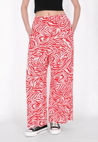 Rood-wit zebra print wijdvallende broeken met een elastische tailleband, voorzien van zijzakken en een lichte stof. Gedragen met zwarte sneakers.
