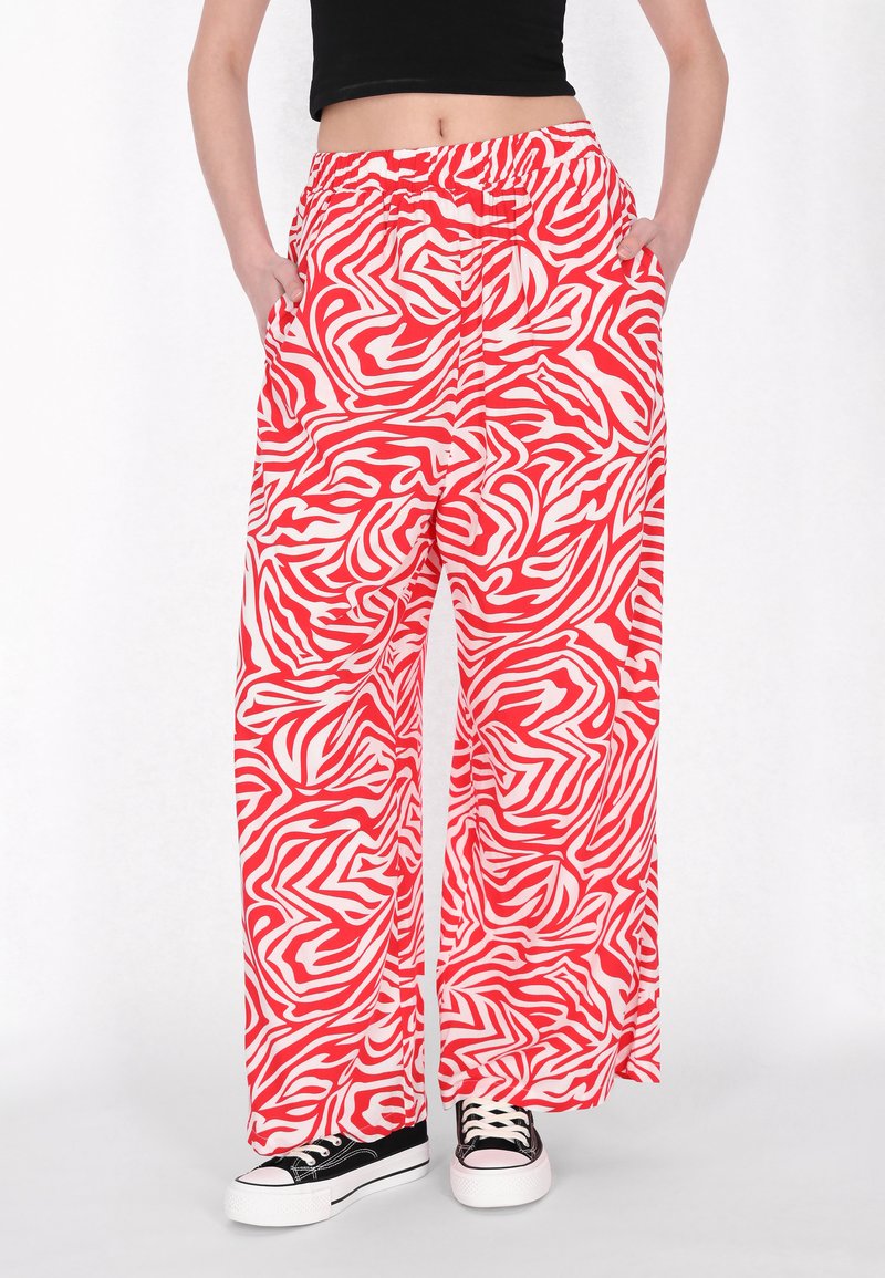 Røde og hvide zebra-print brede bukser med elastisk talje, der har sidelommer og letvægtsstof. Båret med sorte sneakers.