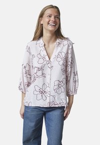 Lyserød bluse med maroon blomsterprint, v-hals og knaplukning. Har trekvartærmer og en afslappet pasform. Kombineret med blå jeans.
