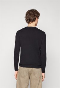 Maglione nero lavorato a maglia con maniche lunghe, scollatura rotonda e orlo a coste. Abbinato a pantaloni beige chiaro, che mettono in risalto un look casual.