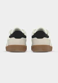 Λευκά και καφέ αθλητικά παπούτσια με μαύρες λεπτομέρειες, με λείο επάνω μέρος, επενδεδυμένο πέλμα και εξωτερική σόλα από καουτσούκ για πρόσφυση.