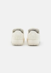 Pár off-white tenisek Puma s texturovanou látkou, zobrazeno zezadu na bílém pozadí.