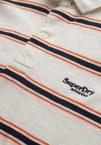 Kortærmet polo shirt i lys beige med vandrette striber i navy og orange. Har en knaplukning og broderet logo på brystet.