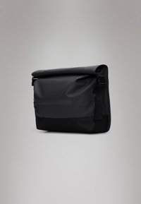 Mala mensageiro preta com parte superior dobrada, feita de material à prova de água. Apresenta um bolso frontal com fecho, alça ajustável e textura suave.