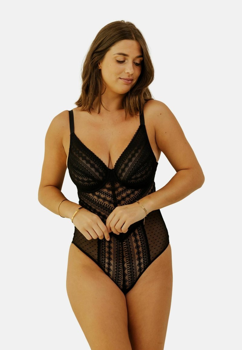 Bodysuit en dentelle noire avec un mesh à motifs, des bords festonnés, des bretelles réglables et un décolleté plongeant. Pois texturés et designs géométriques.