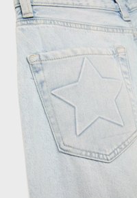 Poche en denim bleu clair avec un motif étoile cousu à l'arrière d'un jean, montrant la boucle de ceinture et les détails de couture.
