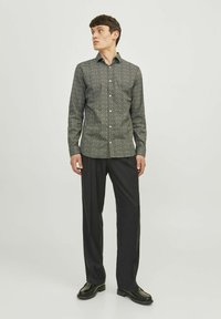 Chemise à manches longues à motif noir et blanc avec un col boutonné, associée à un pantalon noir et des chaussures noires brillantes.