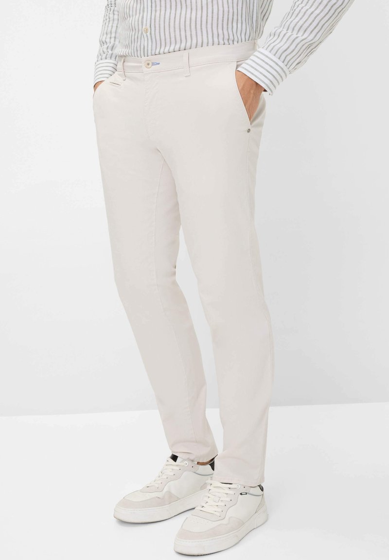 Helle beigefarbene Chinos aus Baumwolle im Slim-Fit, mit Seitentaschen und einer dezenten Textur. Tragen mit weißen Sneakers und einem gestreiften Hemd.