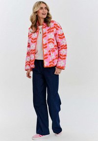 Kvetinová vzorovaná ružová prešívaná bunda s oranžovým zipsom, v kombinácii s tmavomodrými širokými nohavicami a svetloružovými teniskami. Svetlý a farebný dizajn.