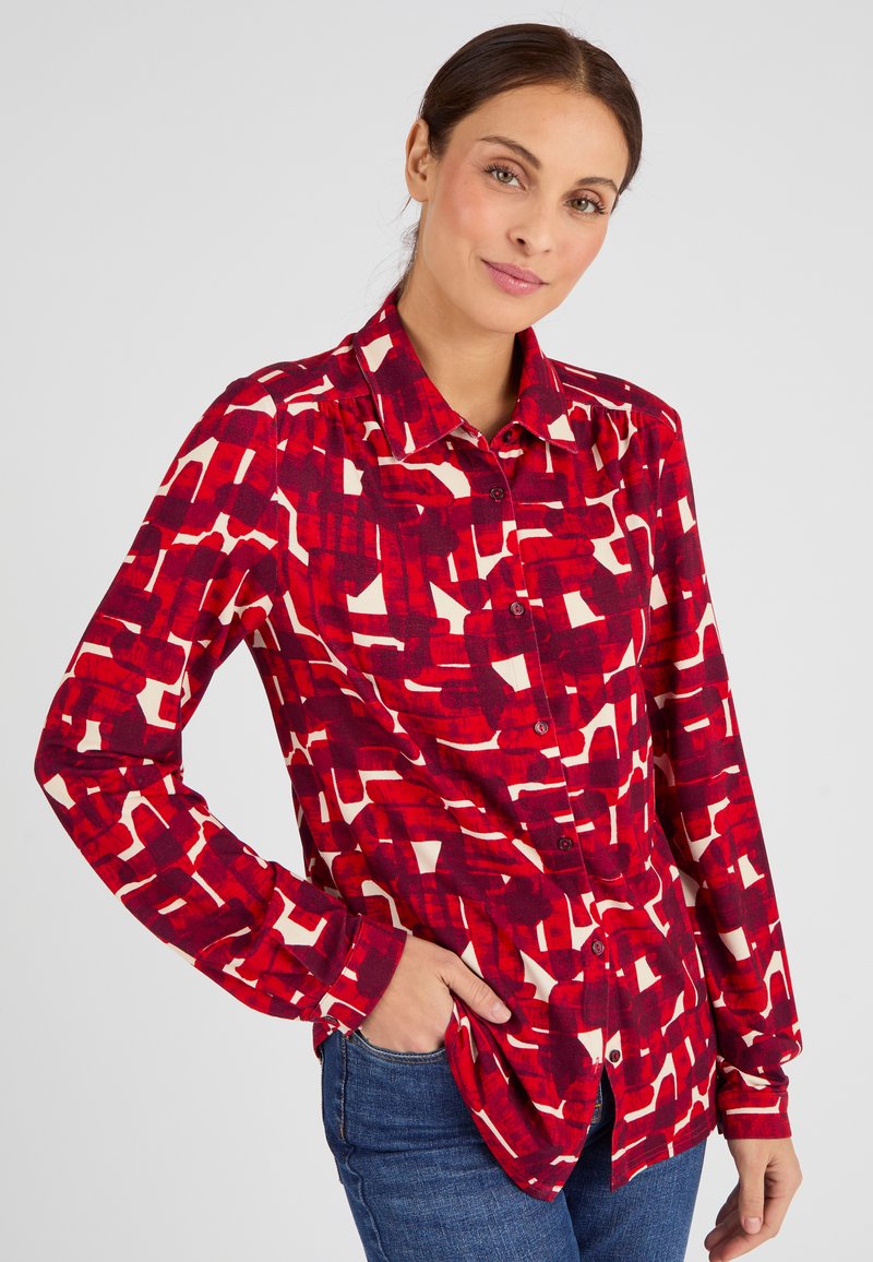 Camicia a maniche lunghe con pattern rosso e crema, dotata di collo e vestibilità rilassata. Tessuto morbido.
