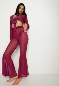 Conjunto de tres piezas en magenta transparente que incluye un top corto con un lazo, pantalones acampanados y acentos estampados en el bañador.